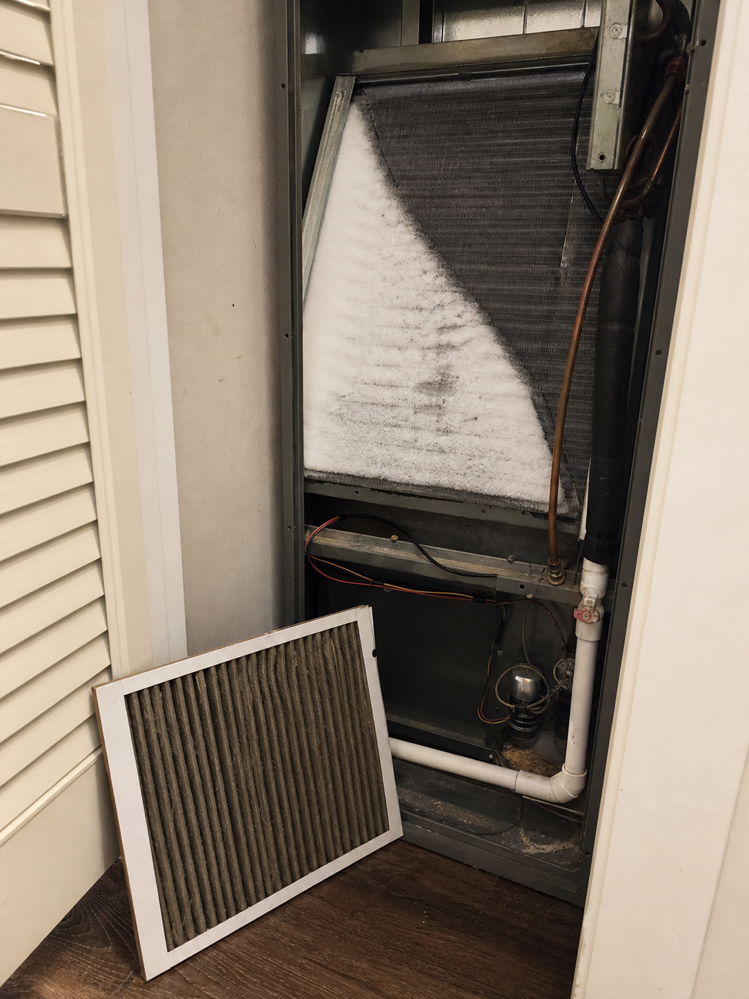 Indoor air handler closet with the front panel removed showing an evaporator coil partially covered in ice