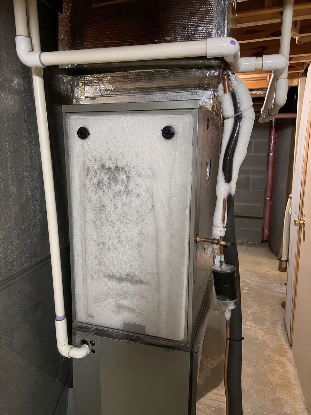 Indoor air handler in a residential basement with ice visibly built up on the copper refrigerant lin (why is my AC suddenly blowing warm air in St. Louis)