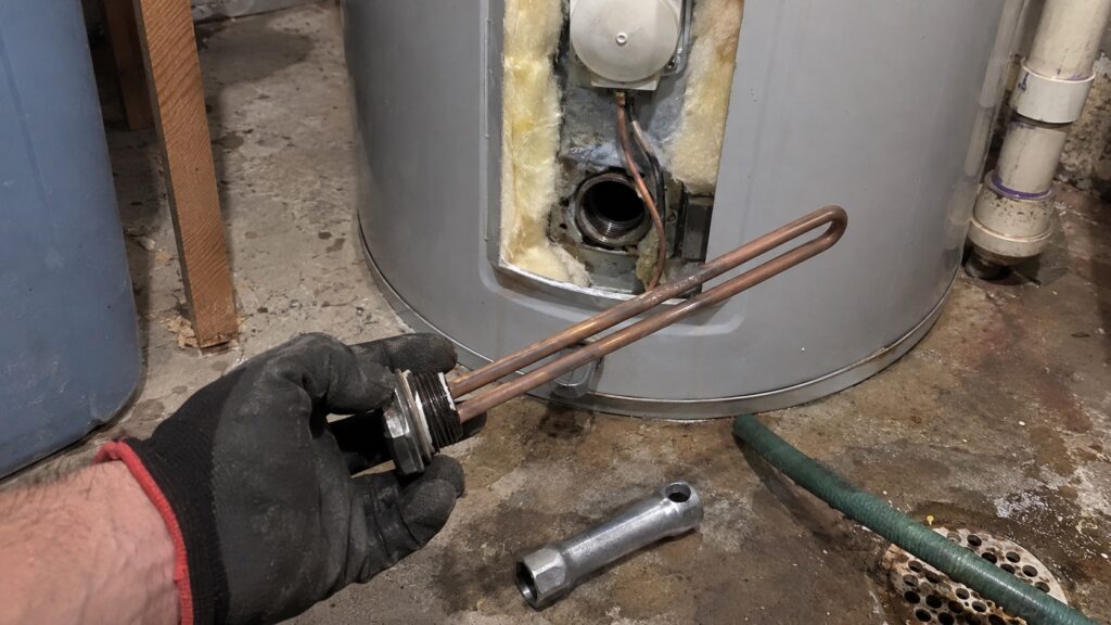 Worn electric water heater element pulled out of the tank during a repair, with the element wrench on the floor